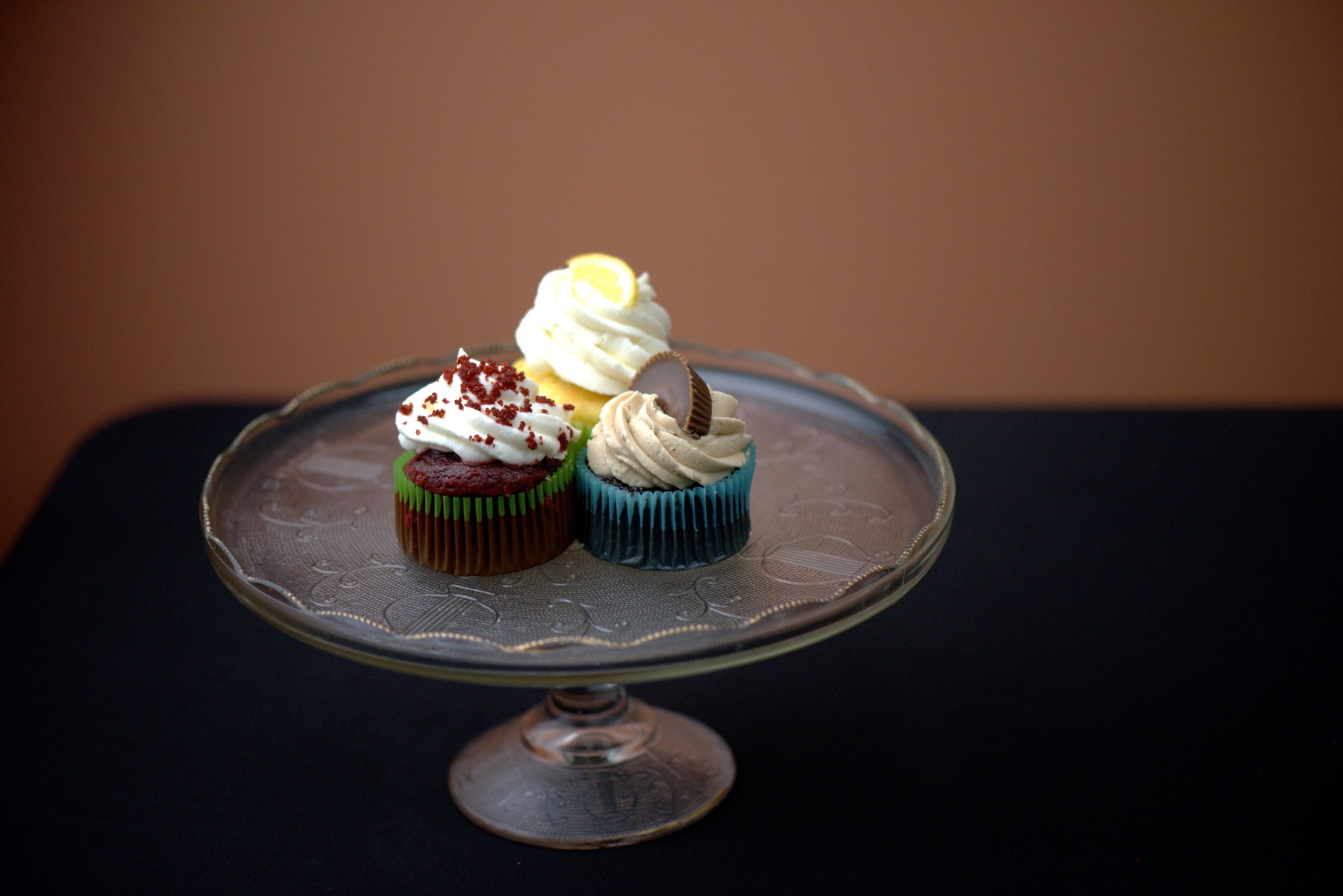 A trio of cupcakes displayed on a glass pedestal cake stand